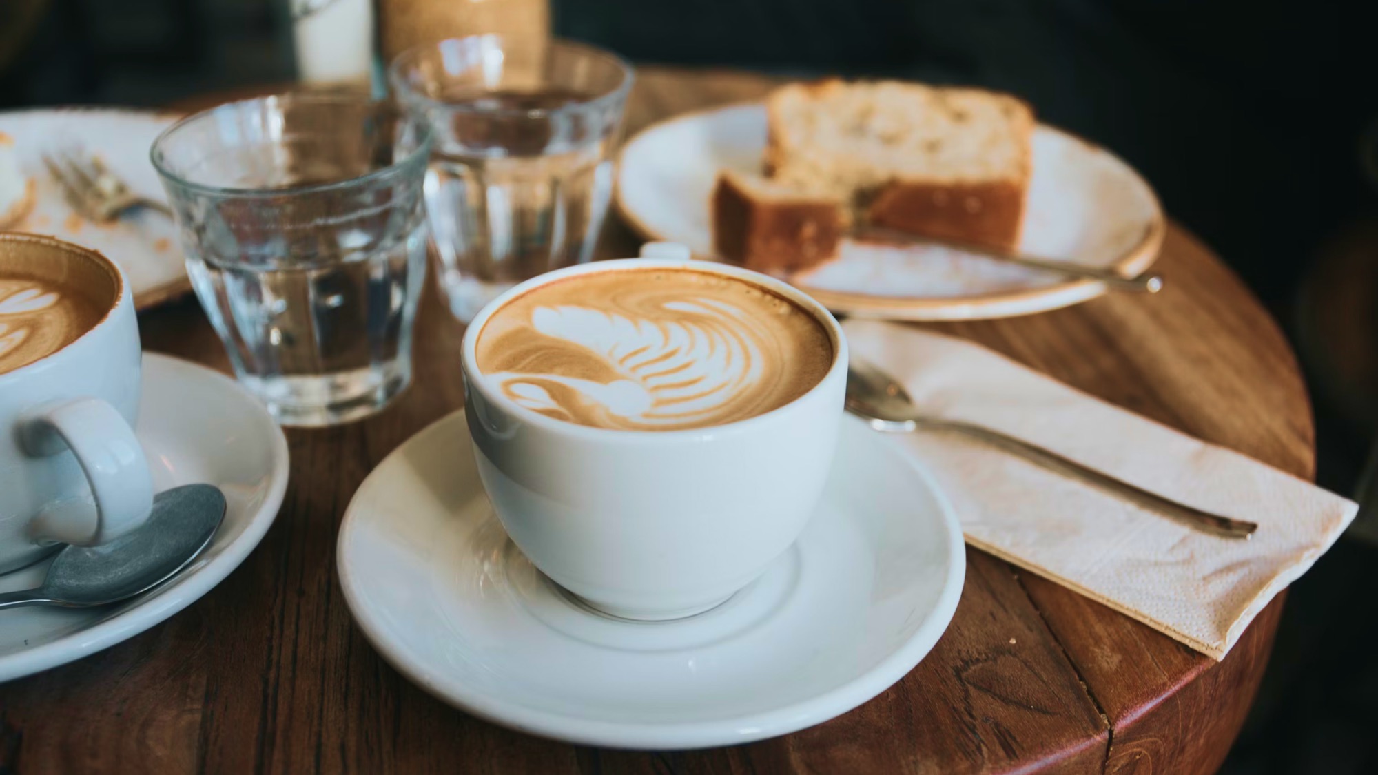 Flat white with latte art beside a slice of cake on a wooden table